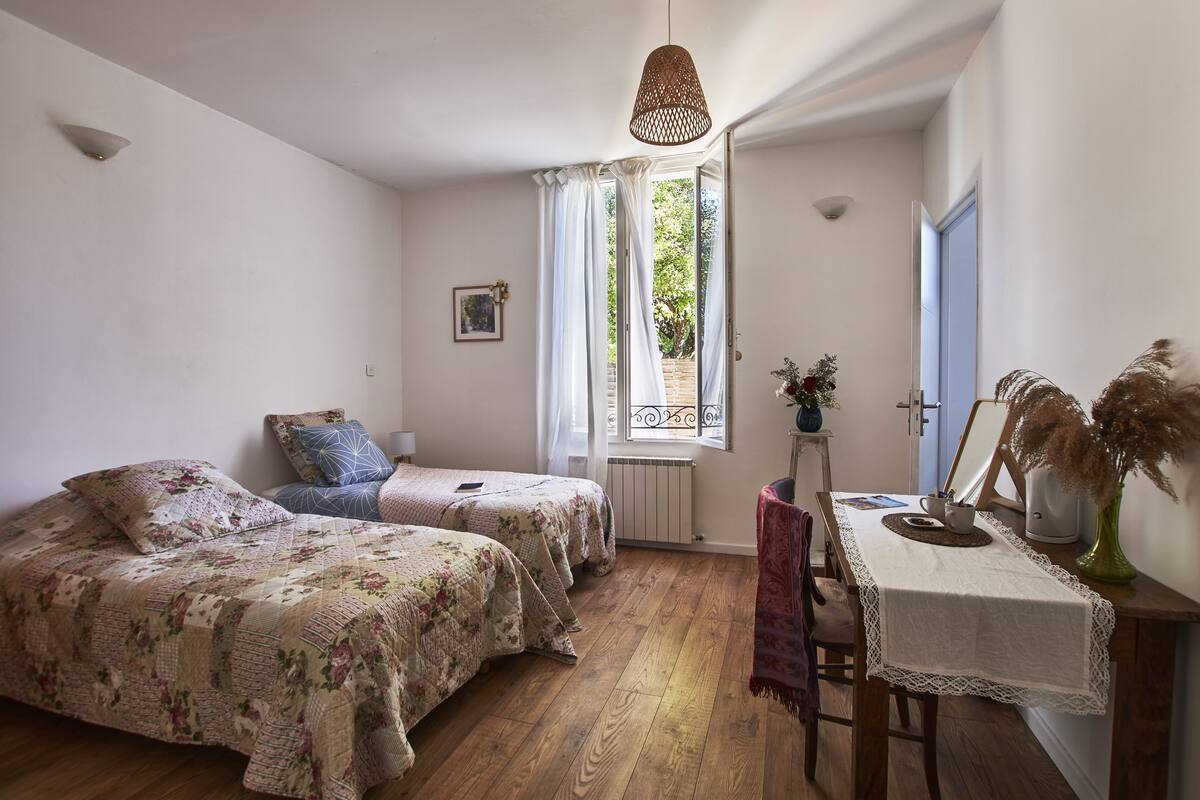 A bedroom with two beds, a table with a vase, and a window with curtains.