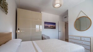 A neatly arranged bedroom with a bed, a wardrobe, a mirror, and a cityscape picture on the wall.
