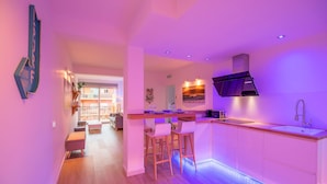 A modern kitchen with a bar area, wooden flooring, and a view to the living area.