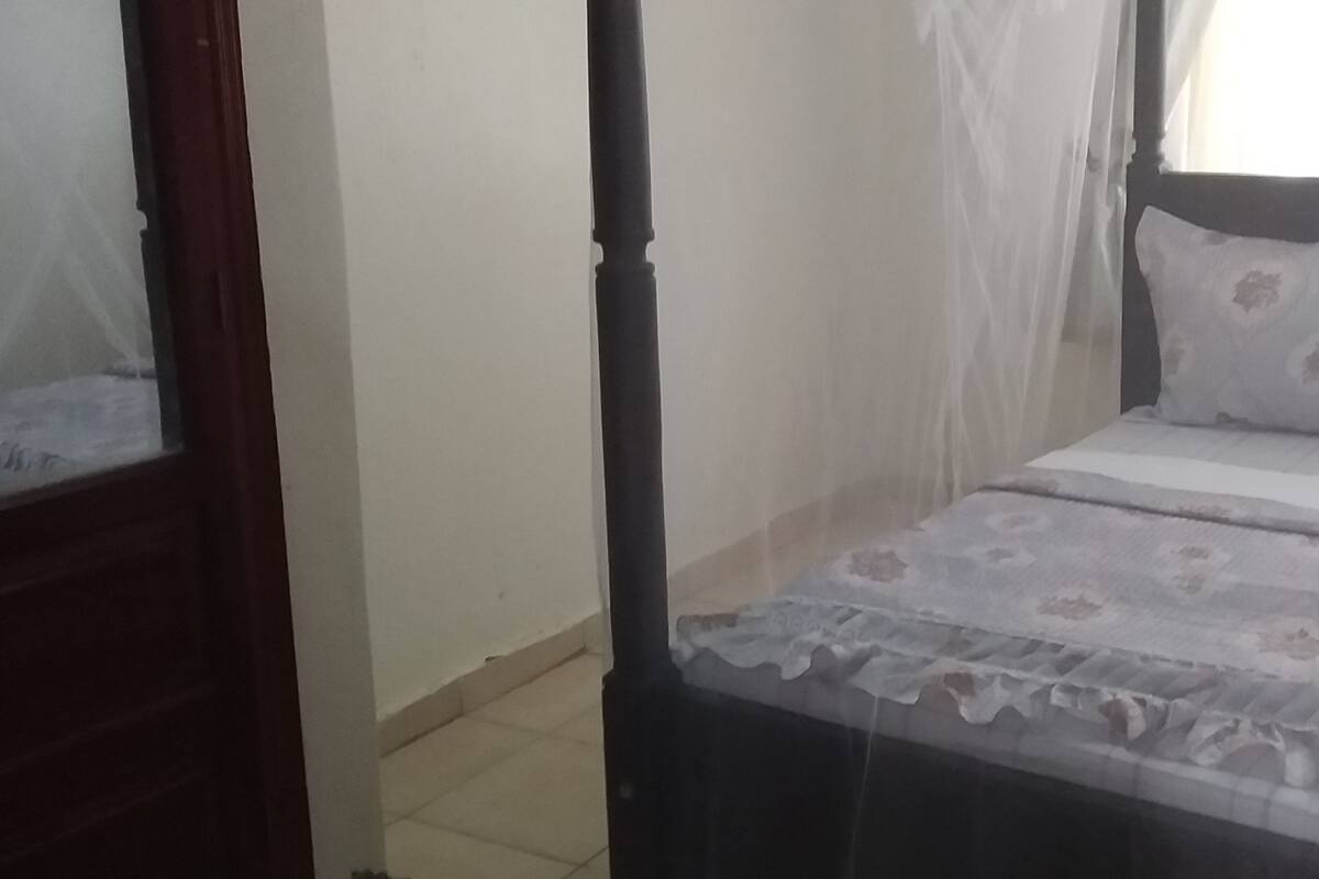 A bedroom with a bed, a window with curtains, and a door.