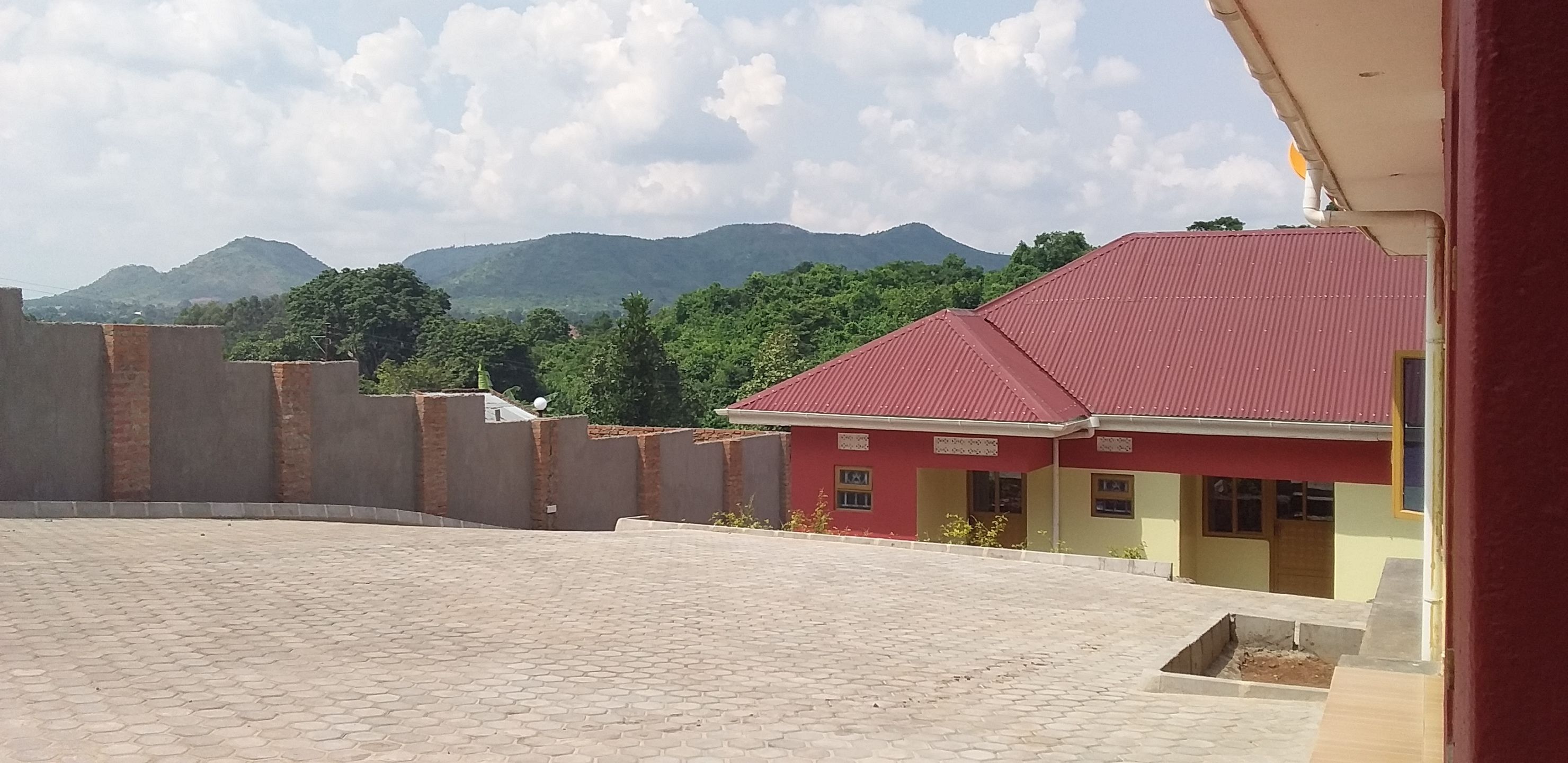 A building with a red roof, surrounded by a paved courtyard and a low brick wall.