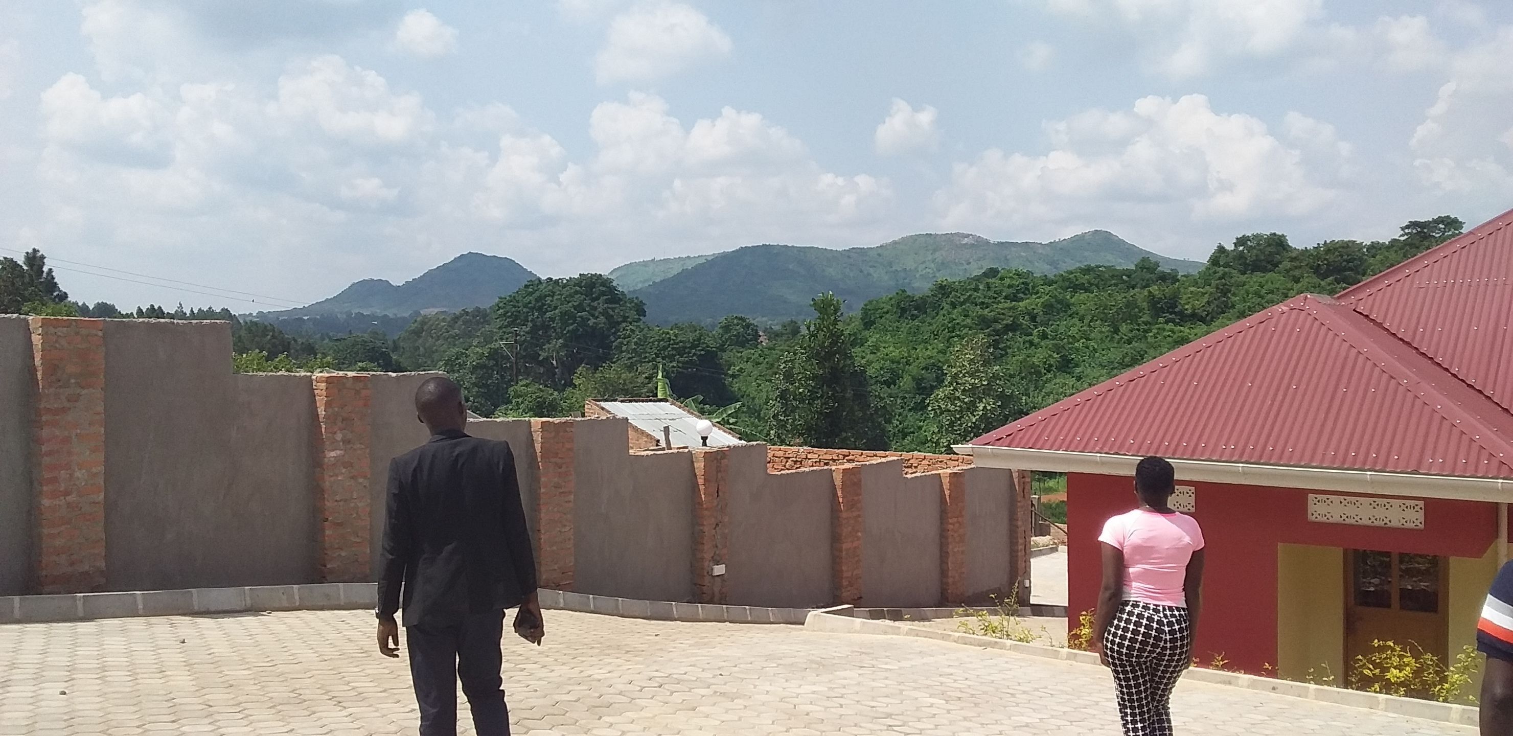 Une cour pavée, un mur en briques, un bâtiment à toit rouge et une chaîne de montagnes en arrière-plan.