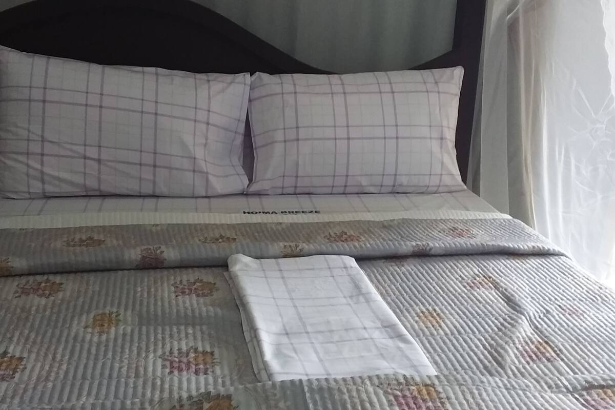A bed with a floral-patterned bedspread, a white pillow, and a white blanket.