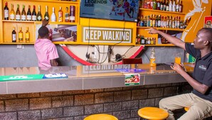 A bar area with stools, a counter, and shelves stocked with bottles. - Hoima Breeze Hotel (Hoima)