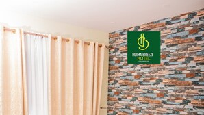 A neatly made bed with pillows and a blanket, a wooden headboard, a patterned wall, and a curtain. - Hoima Breeze Hotel (Hoima)