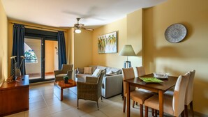 Una sala de estar con sofá, mesa de comedor, sillas, ventilador de techo y un cuadro en la pared.