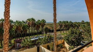 Un balcón con vista a palmeras y una playa lejana.