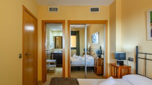 Habitación de hotel con cama, mesita de noche, espejo, televisor y baño visible a través de una puerta abierta.
