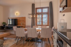 A modern living room with a TV, seating, a dining area, and a kitchen.