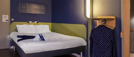 Una cama bien hecha con sábanas blancas, un cabecero verde y una mesita de noche de madera con una lámpara.