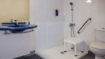 A bathroom with a white toilet, a blue sink with a chrome faucet, a shower with a handheld showerhead, and a white step stool.