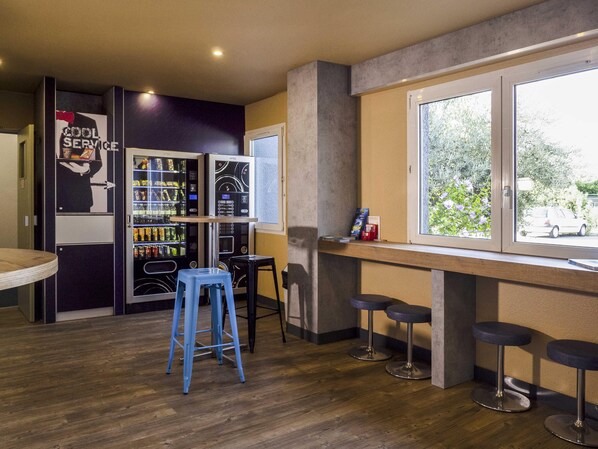 Un espace bar moderne avec des tabourets, un distributeur automatique et une fenêtre donnant sur l’extérieur.