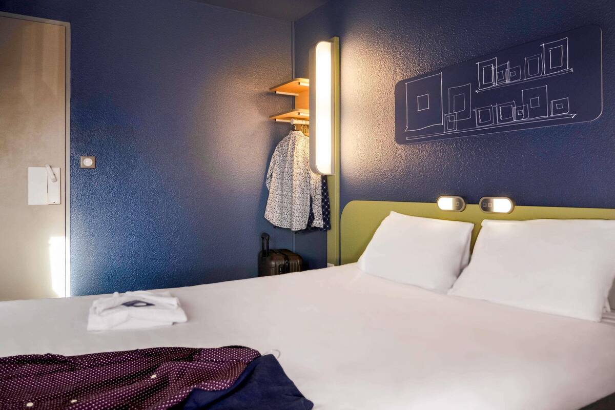 A hotel room with a bed, a nightstand, a wall-mounted light, and a towel rack.