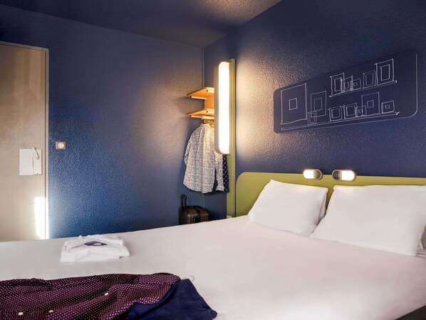 Una habitación de hotel con cama, mesita de noche, lámpara de pared y perchero.