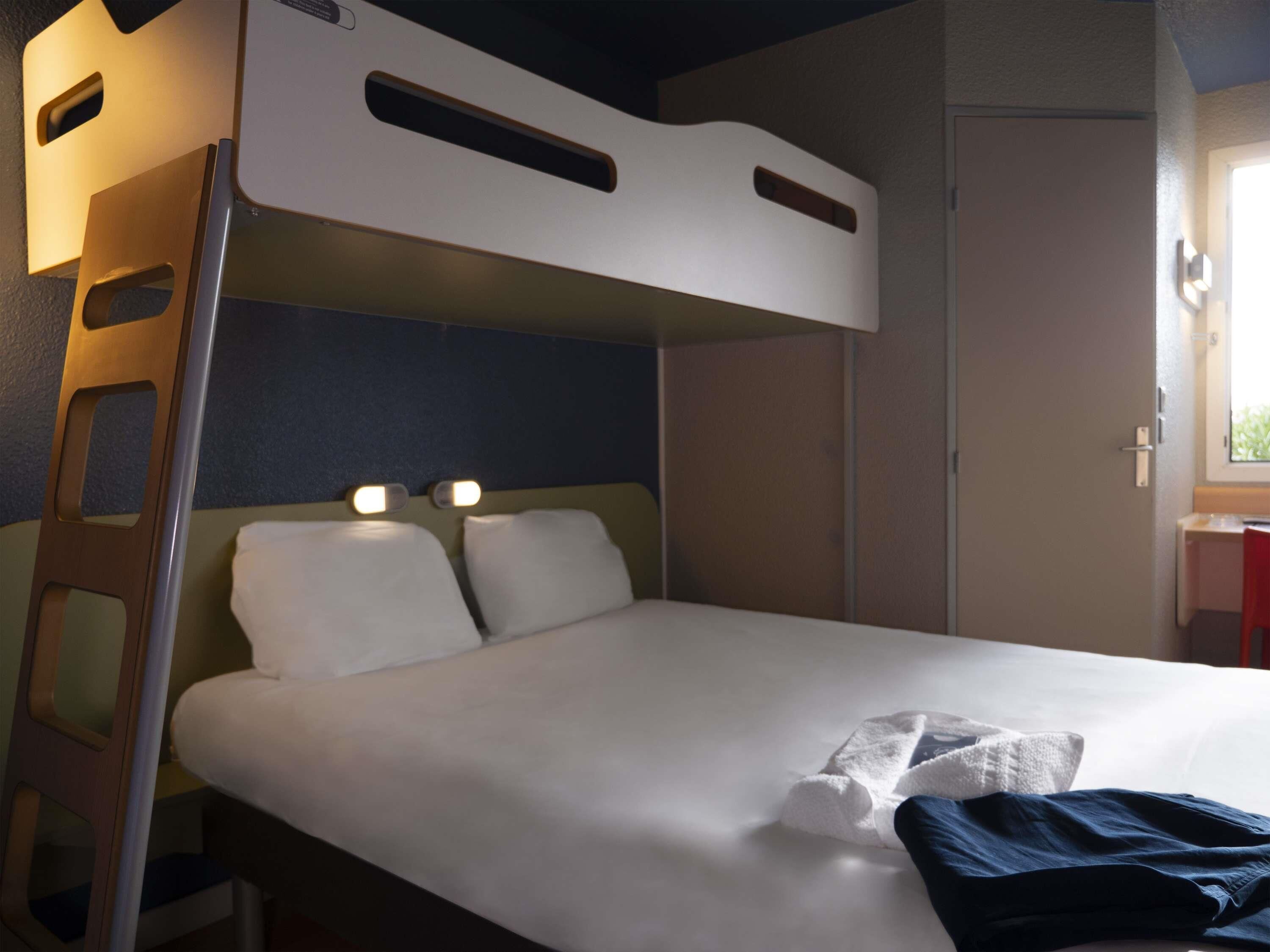A bunk bed with a ladder, a bedside table, and a window with daylight.