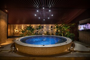 Un jacuzzi con un muro de piedra de fondo, rodeado de plantas y cubierta de madera.
