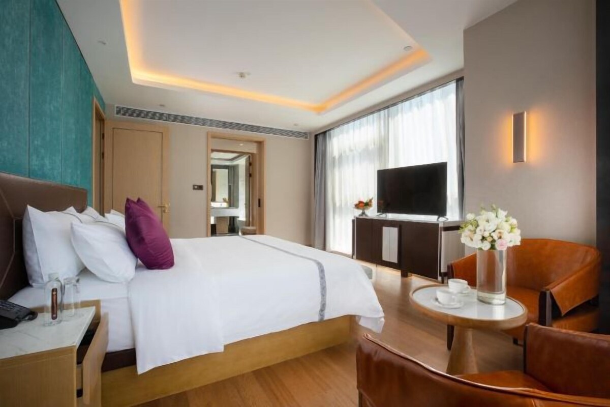 Une chambre d’hôtel comprenant un lit, un bureau avec une chaise, une télévision et une petite table sur laquelle est posé un vase de fleurs.