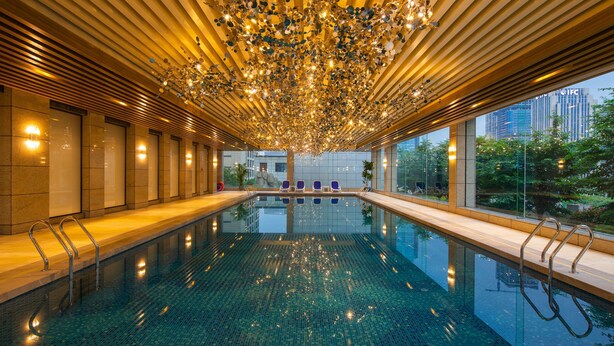 Una piscina interior moderna amb superfície reflectant, envoltada de gandules i un sostre decorat amb llums penjants.