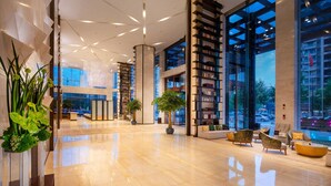 Un vestíbul espaiós amb un disseny modern, que inclou una gran biblioteca, zona de seients i grans finestres amb vistes a la ciutat.