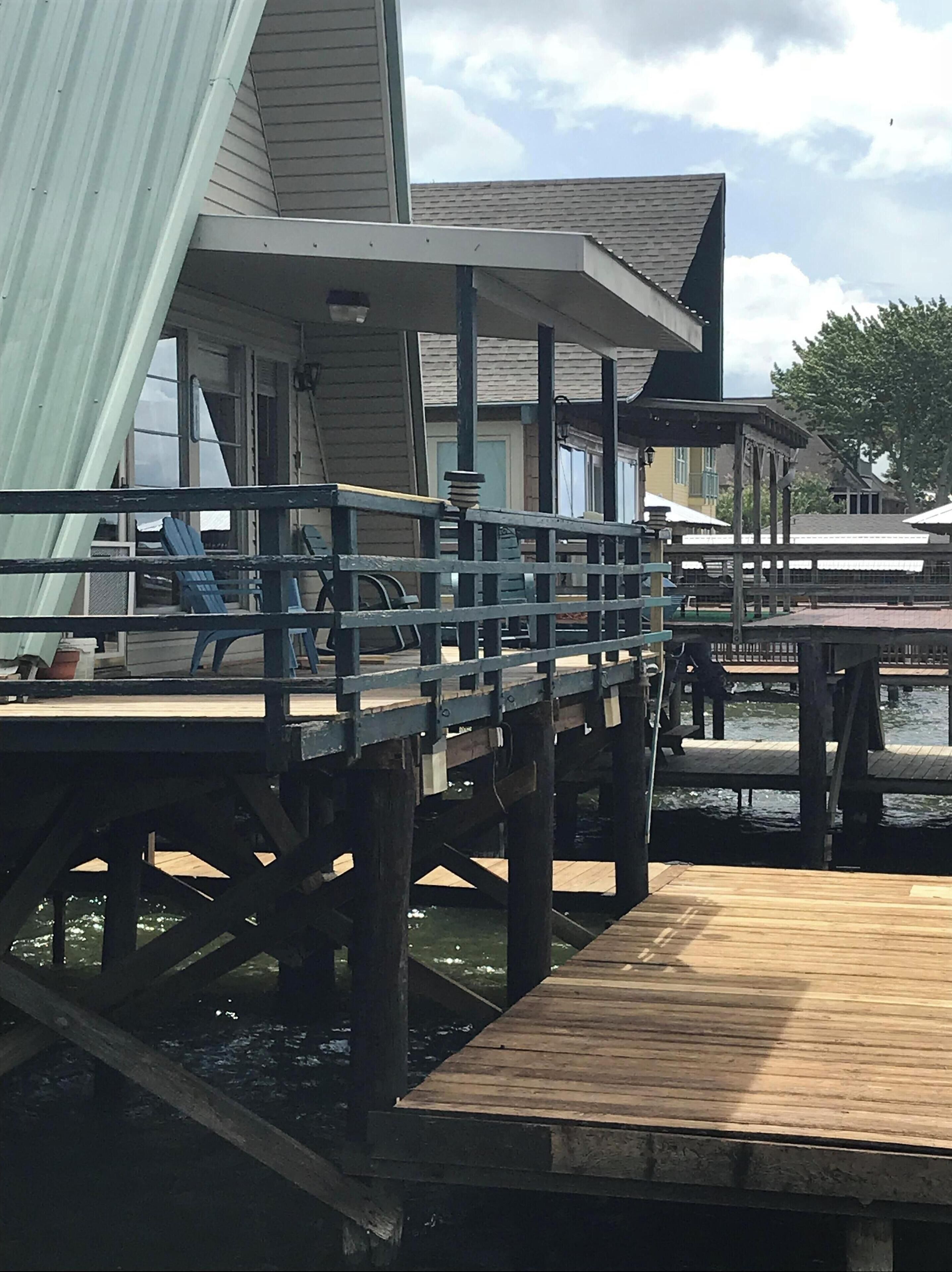 A wooden dock extending into a body of water, with a covered seating area and a building in the background.
