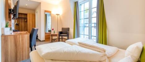 A hotel room with a bed, a desk, a chair, a TV, and a window with curtains.