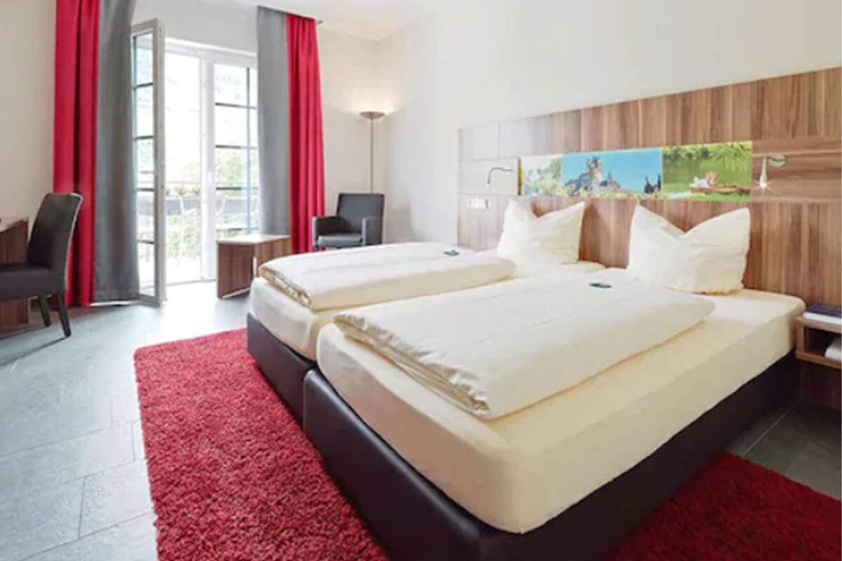 Una habitación de hotel con dos camas, un escritorio, una silla y un cuadro en la pared.