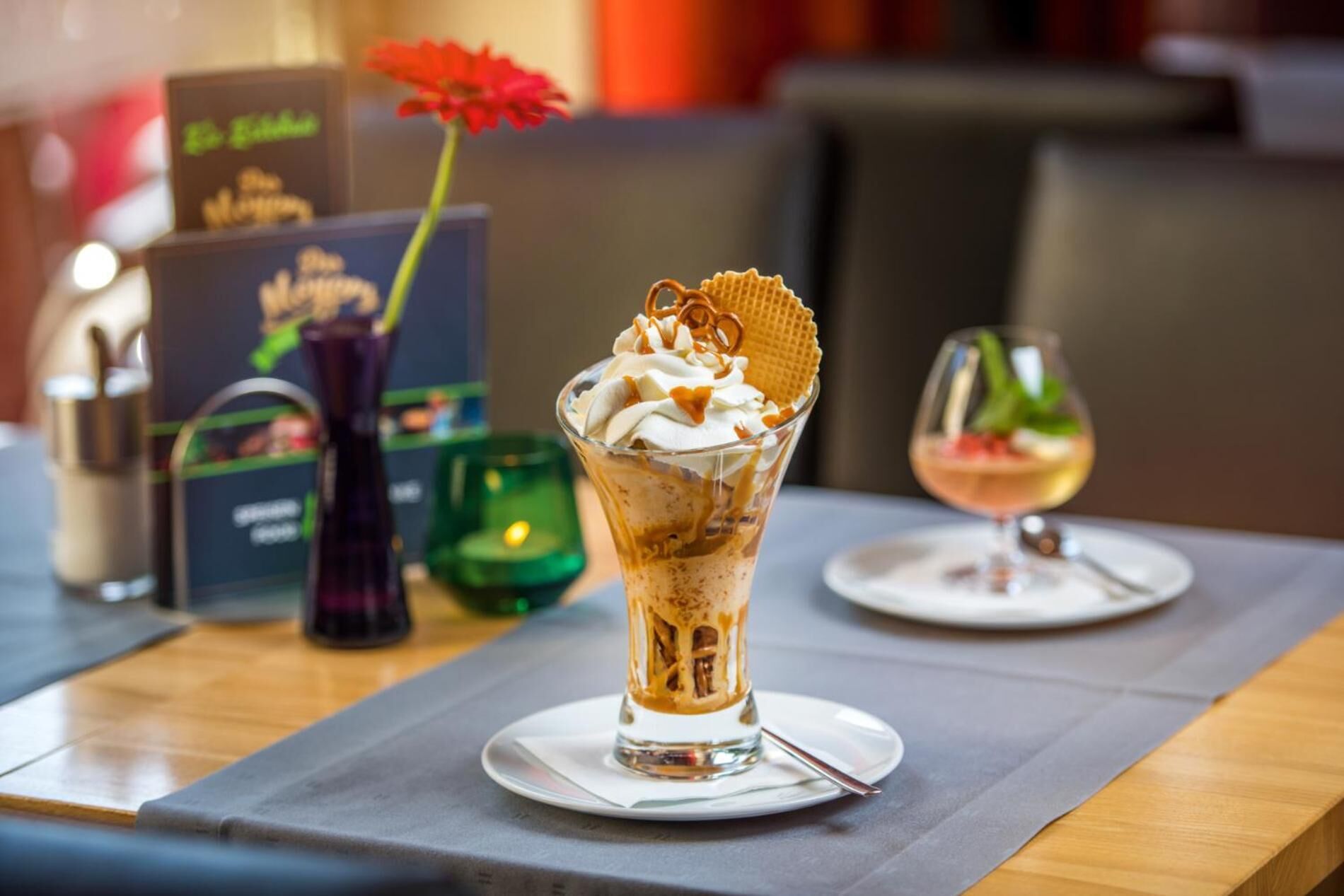 Postre con crema batida y una galleta sobre un vaso, una vela y un menú en una mesa.