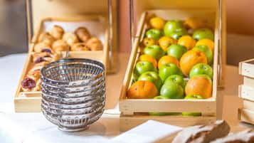 Una mesa con cajas de madera llenas de frutas y pasteles, además de un bol de vidrio.
