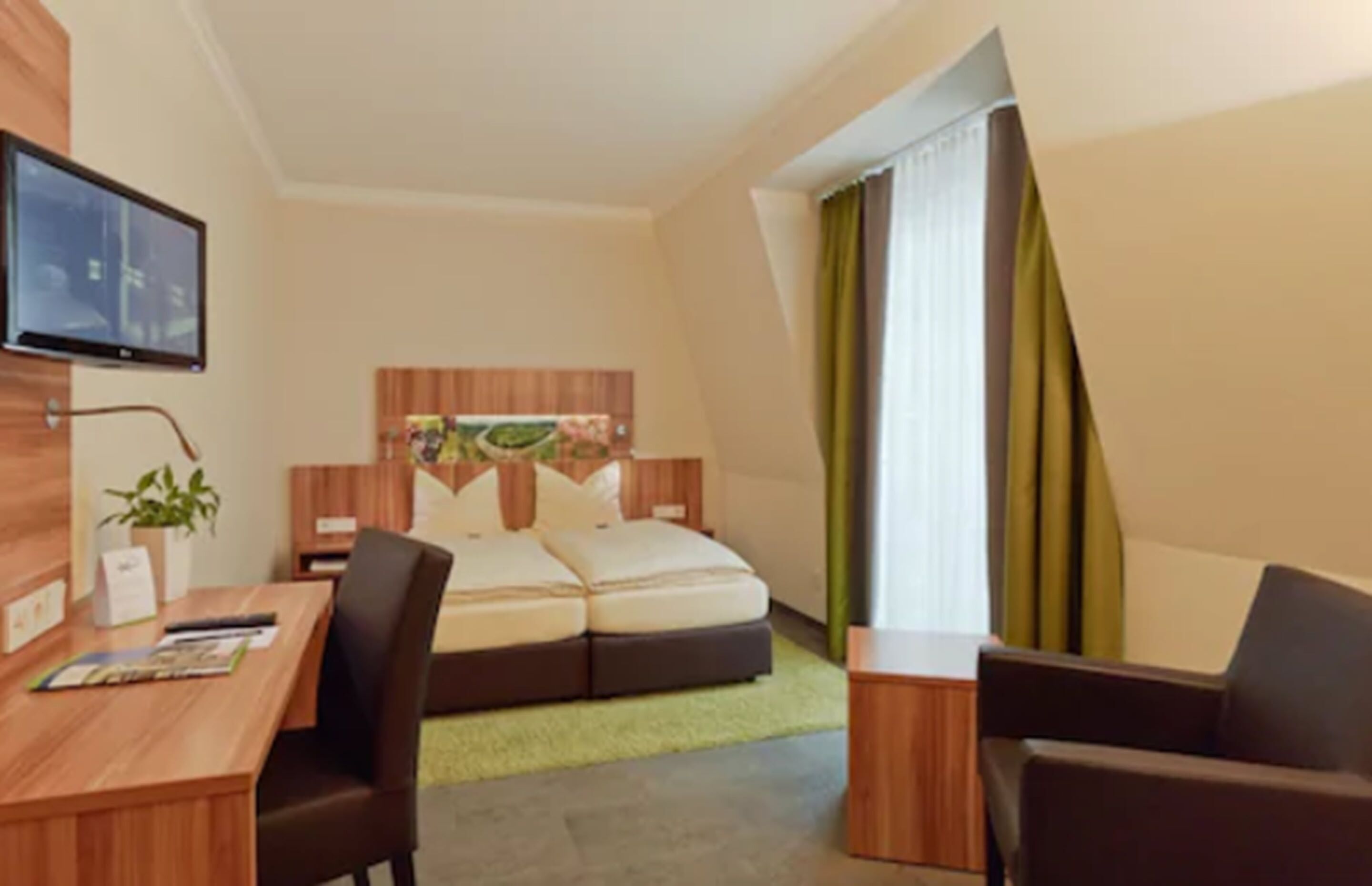 Habitación de hotel con cama, escritorio, silla, televisor y ventana con cortinas.