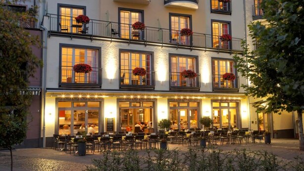 Un hotel con varios balcones, una entrada bien iluminada y zona de estar al aire libre.