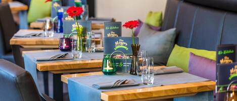 Un restaurant avec des tables dressées pour le service, des menus et des décorations florales en guise de centre de table.