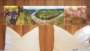 Habitación de hotel con dos camas blancas, cabecera de madera y una pared decorada con tres cuadros: uvas, paisaje fluvial y flores de cerezo.