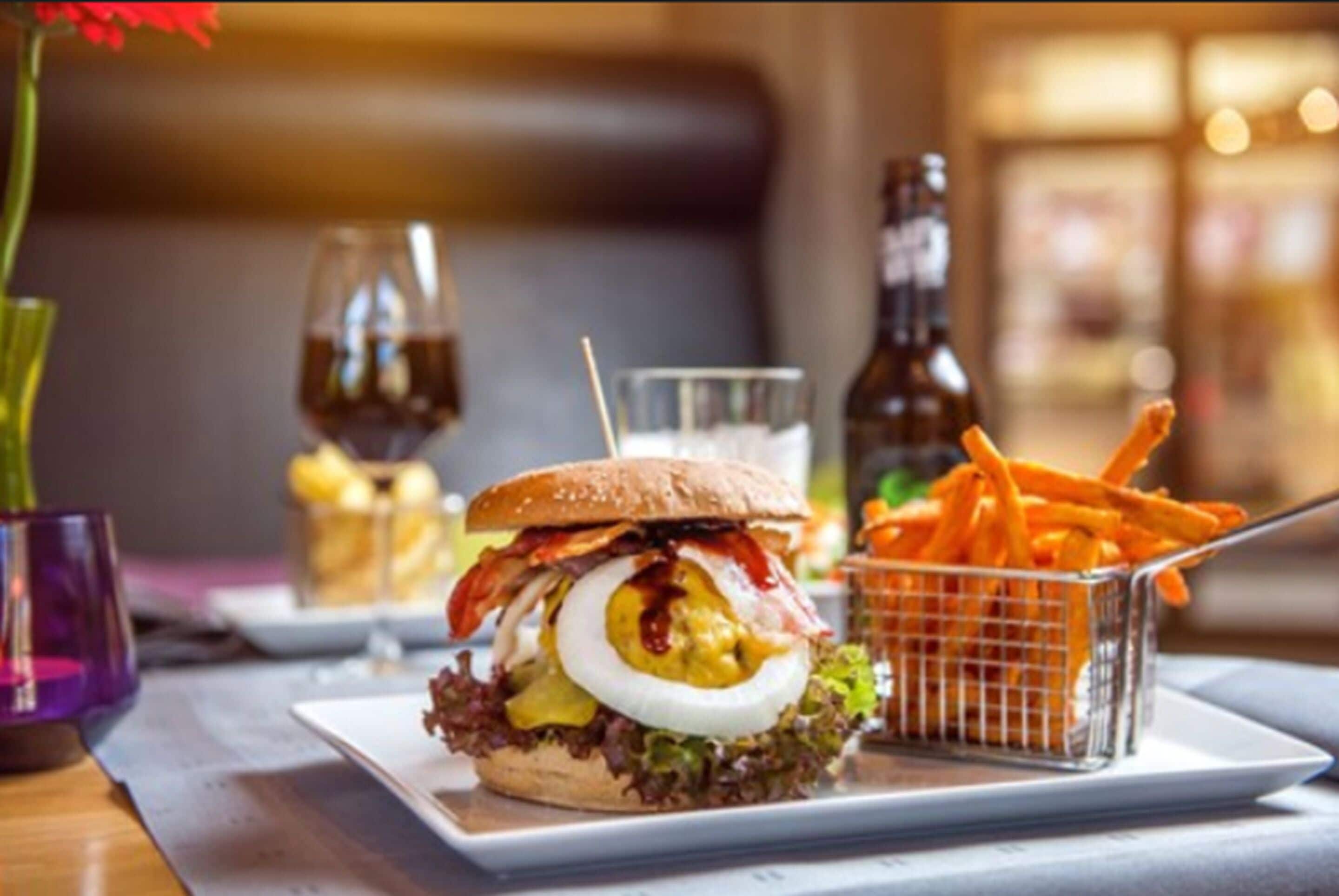 Een hamburger met frietjes op een bord, een biertje en een glas water op een tafel.