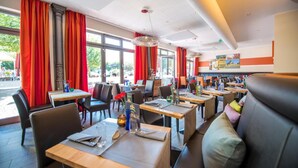 Un restaurante con varias mesas y cabinas, amplias ventanas con cortinas rojas y una decoración de estilo moderno.