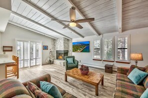A spacious living room with a fireplace, a ceiling fan, and a large window with blinds. - Tahoe gem! Spacious Lake Village condo close to beaches & ski area! (Zephyr Cove)