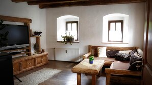 A cozy living room with a wooden TV stand, a sofa, a coffee table, and two windows with plants. - Tiefala's Eck (Stubenberg)