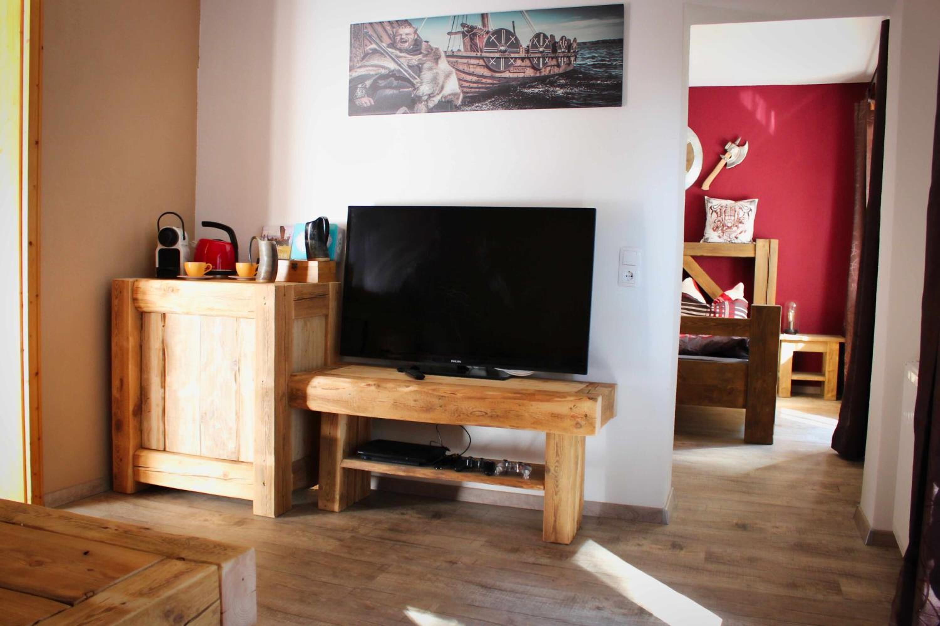 Un salon avec un meuble de rangement en bois pour l’équipement audiovisuel, un téléviseur à écran plat et un tableau représentant un navire accroché au mur.