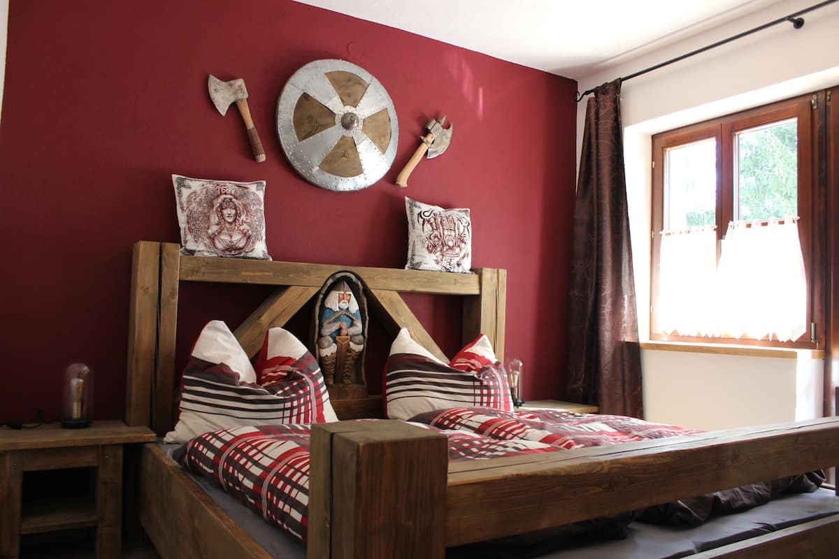 Ein rustikaler Raum mit einem Holzbett, einem Schild und zwei Äxten an der Wand.