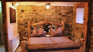 A rustic wooden bed with a stone wall backdrop, a lantern above, and a framed picture on the wall. - Tiefala's Eck (Stubenberg)