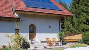 A house with a sloped roof, solar panels, a front door, and a small patio with two chairs. - Tiefala's Eck (Stubenberg)