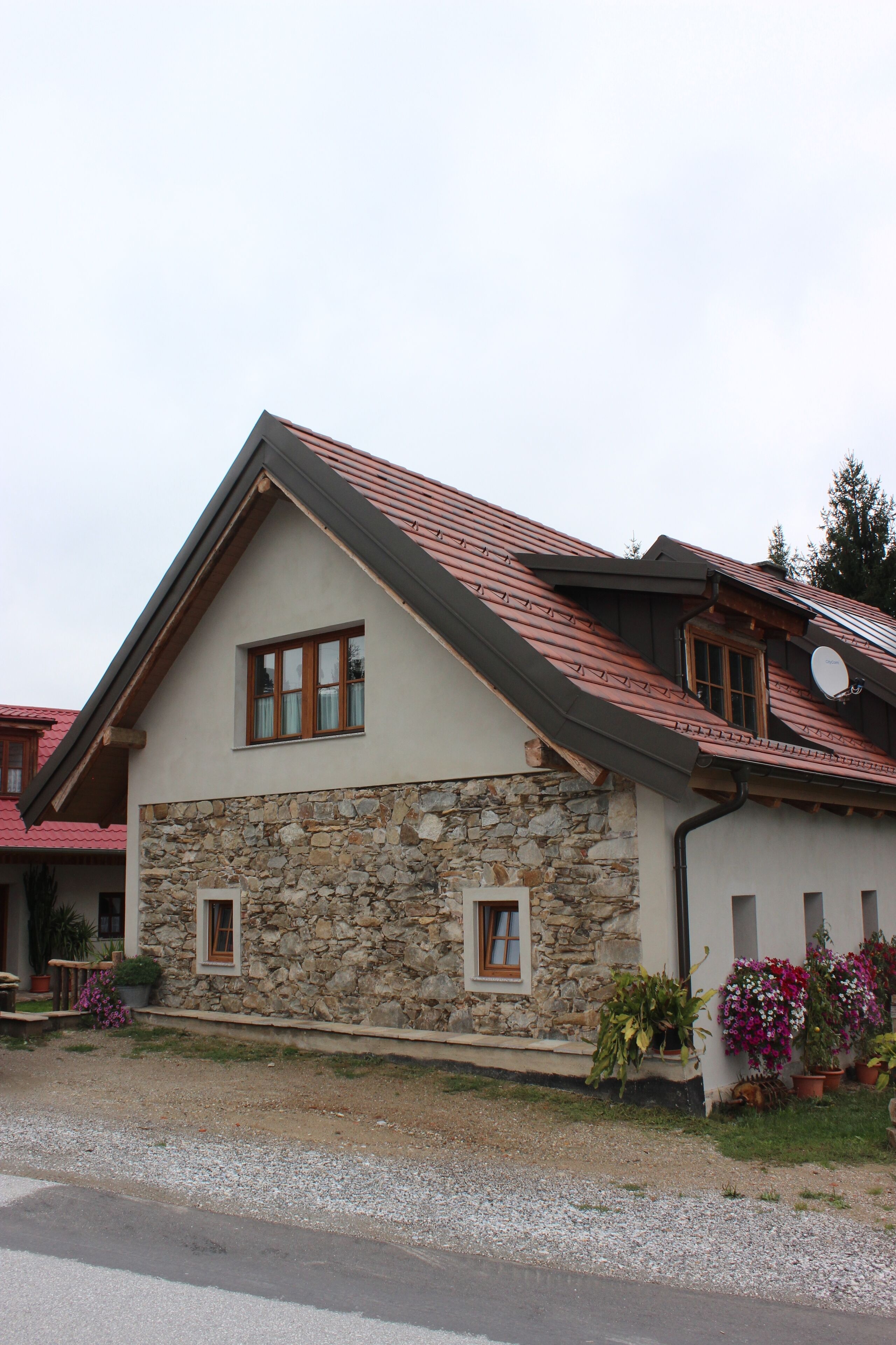 A two-story house with a stone facade, a sloped roof, and a satellite dish.