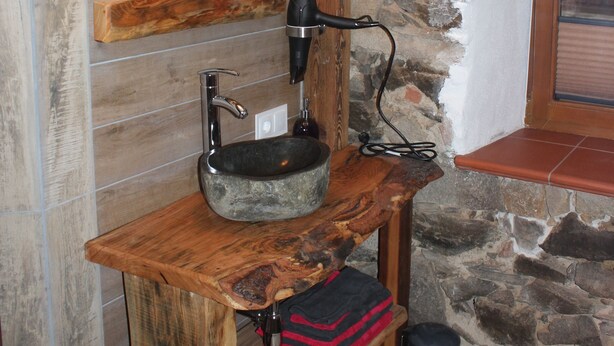 A rustic bathroom with a stone sink, wooden vanity, and a mirror with a wooden frame. - Tiefala's Eck (Stubenberg)