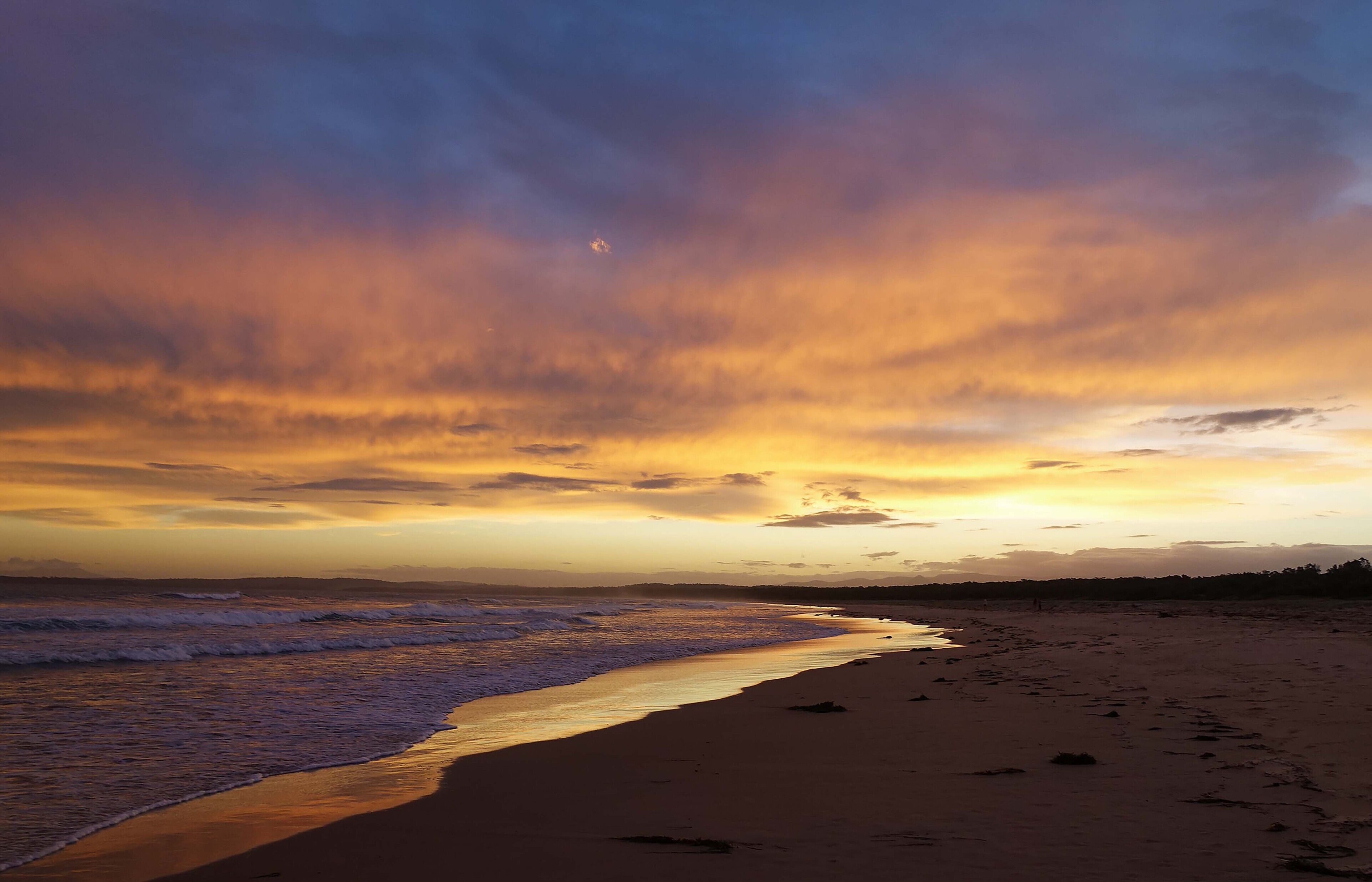 Una playa con un atardecer, olas y cielo despejado.