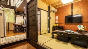 A traditional Japanese-style room with tatami flooring, a low table with a tea set, and a television mounted on the wall. - KumoMachiya Takoyakushi (Kyoto)