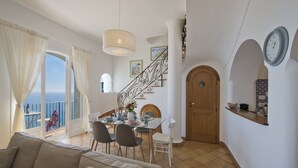 A spacious living room with a balcony, a dining area with a table set for four, and a staircase leading to another level. - Casa Malu' (Praiano)