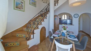 A dining area with a glass table, chairs, and a staircase with ornate railings. - Casa Malu' (Praiano)