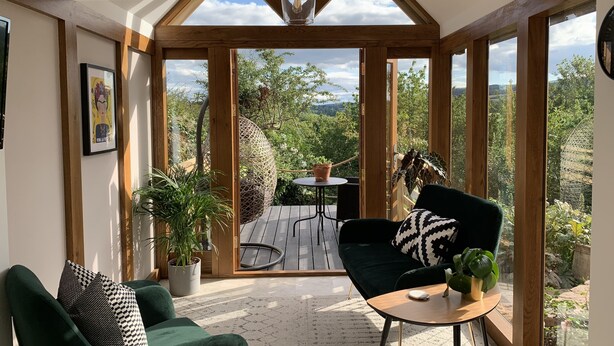 A cozy room with a green sofa, a small round table, and a view of a garden through large windows. - Boutique garden apartment with decking and views (Ludlow)
