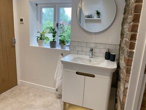 A bathroom with a white sink, a mirror, a window with plants, and a brick wall. - Boutique garden apartment with decking and views (Ludlow)