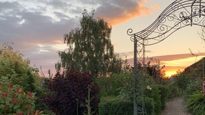 A garden pathway leading to a gate, surrounded by various plants and potted plants. - Boutique garden apartment with decking and views (Ludlow)