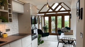 A modern kitchen with white cabinetry, a built-in oven, and a dining area with a table and chairs. - Boutique garden apartment with decking and views (Ludlow)